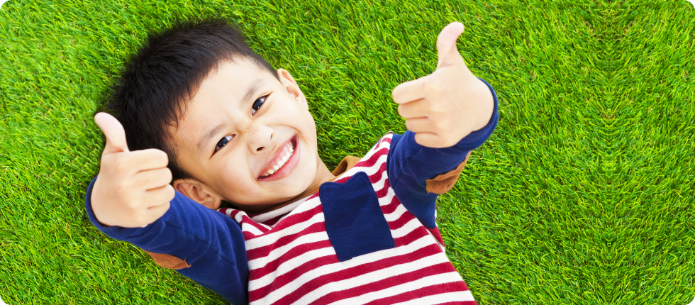 A boy laying on the ground and doing a thumbs up sign